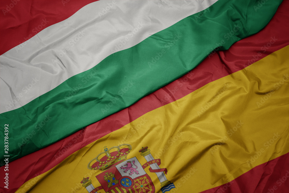 waving colorful flag of spain and national flag of hungary.