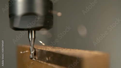 SLOW MOTION, MACRO, DOF: Twisted pieces of excess metal fly off a piece of aluminium during lathing by a CNC drill. Fine cut end mill shaving the side of a matt block of metal. Micro machining process photo