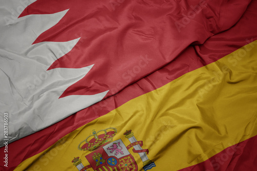 waving colorful flag of spain and national flag of bahrain.