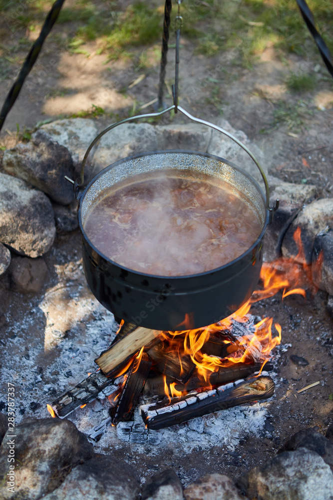 Cooking goulash in a hanged cauldron over the fire in the garden. Cooking goulash in a hanged cauldron over the fire in the garden.