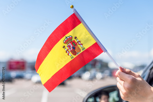 Boy holding Spanish Flag from the open car window on the parking of the shopping mall. Concept