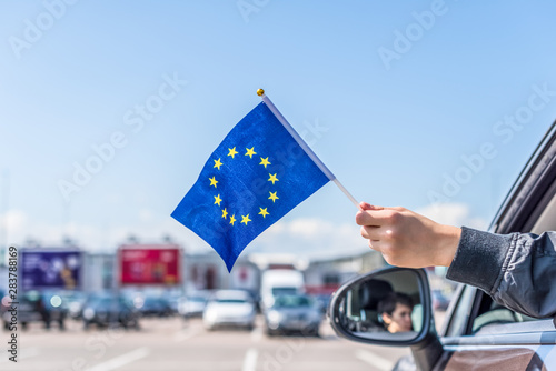 Boy holding Europe or European(EU) Flag from the open car window on the parking of the shopping mall. Concept photo