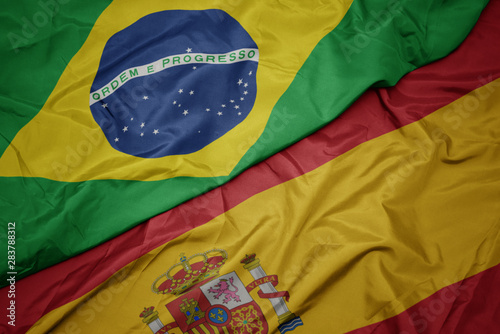 waving colorful flag of spain and national flag of brazil.