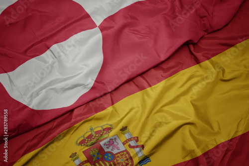 waving colorful flag of spain and national flag of greenland.