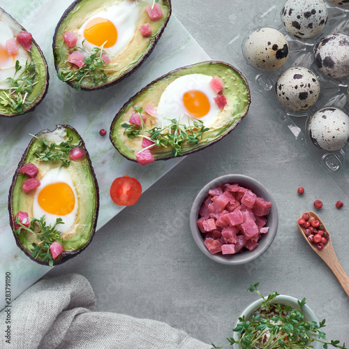 Keto diet dish  Avocado boats with quail eggs  ham cubes and cress sprouts on light stone serving board