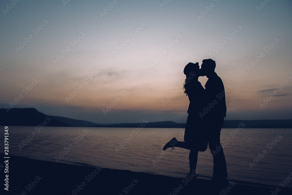 Silhouettes of couple kissing on sunset, lake and mountains background