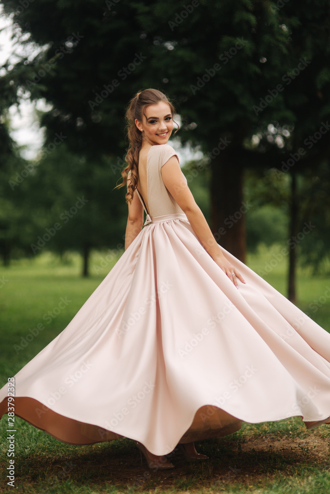Fashionable girl spin around in park. Evening dress