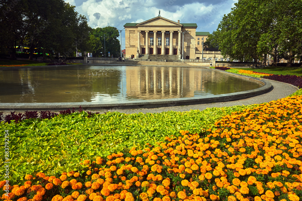 Flower beds, pond and facade of the historic opera building in Poznan.