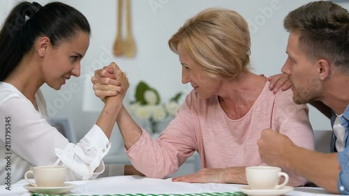 Wife and mother competing hands, fighting for attention of man, arm-wrestling photo