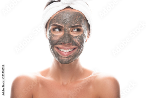 front view of nude young woman in cosmetic hair band with clay mask on face isolated on white