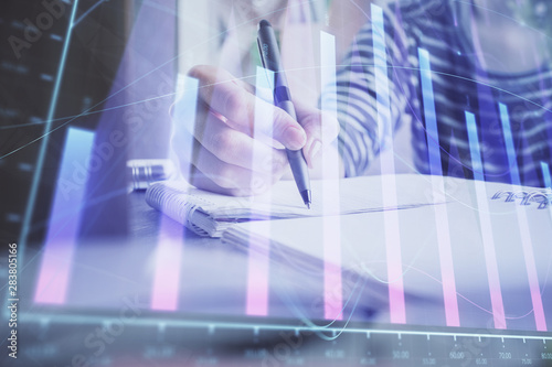 Financial forex graph drawn over hands taking notes background. Concept of research. Double exposure