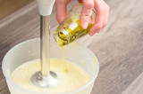 close-up whipping the mixture of homemade mayonnaise with a blender in a plastic bowl. olive oil