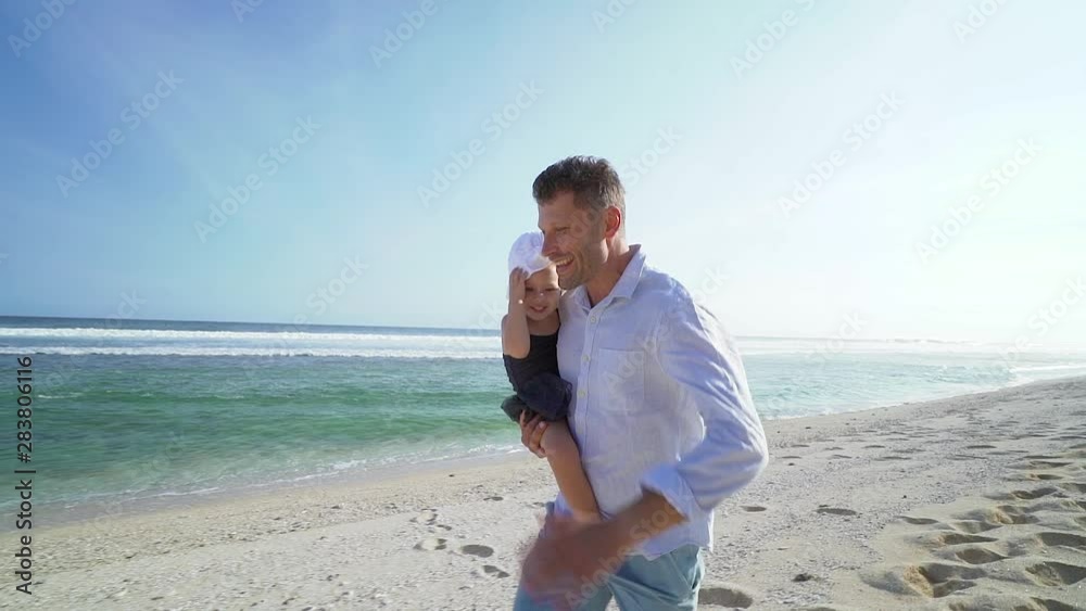 Happy smiling father holds cute daughter in hands and running on the beach at sunny day Happy smiling father holds cute daughter in hands and running on the beach at sunny day
