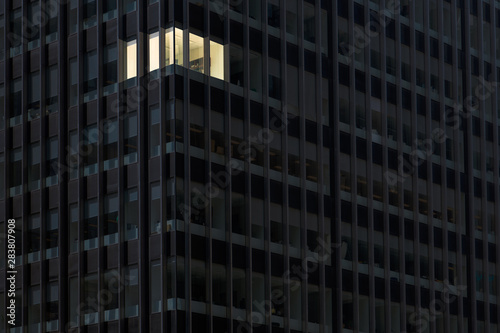 Corner office with lights on and windows glowing in a darkened office building at night indicating someone working overtime late at night