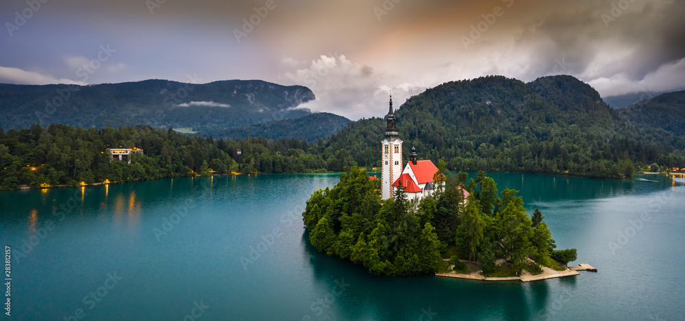 Fototapeta premium Bled, Slovenia - Dramatic sky and clouds above Lake Bled (Blejsko Jezero) with the Pilgrimage Church of the Assumption of Maria on a small island and Julian Alps at background on a beautiful morning