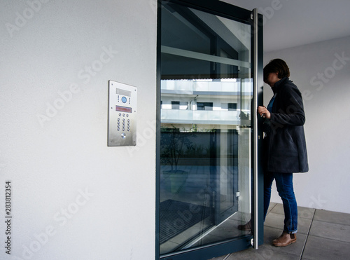 Side view of woman entering modern apartment building with glass door and modern intercom system photo
