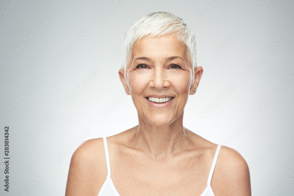 Beautiful smiling senior woman with short gray hair posing in front of gray background. Beauty photography. Beautiful smiling senior woman with short gray hair posing in front of gray background. Beauty photography.