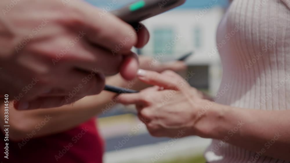 Young people standing in row showing modern mobile phones outdoors at sunlight. Happy friends busy typing on smartphone gadgets in leisure time on urban background. Young people standing in row showing modern mobile phones outdoors at sunlight. Happy friends busy typing on smartphone gadgets in leisure time on urban background.