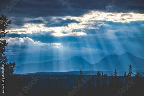 Sun streaks through clouds over mountain landscape at dusk photo