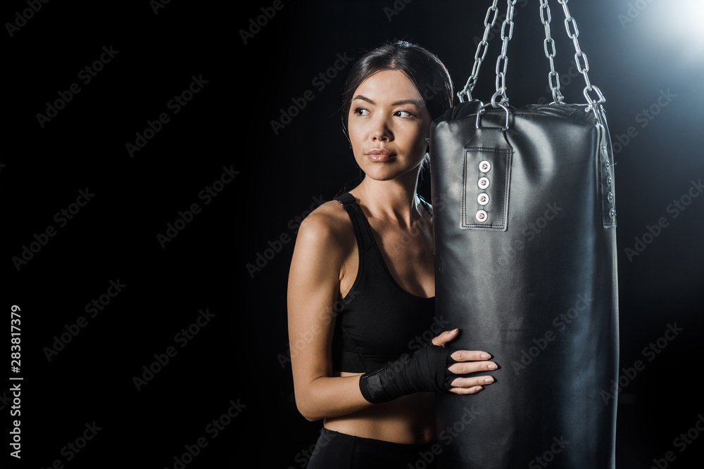 young woman standing near punching bag isolated on black