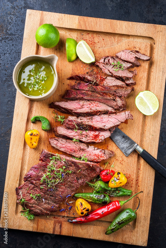 Modern design barbecue dry aged wagyu bavette de flanchet steak with chili and chimichurri sauce as top view on a wooden cutting board photo