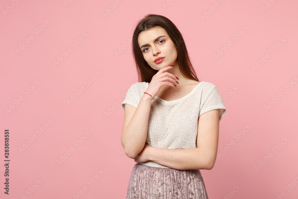 Obraz premium Pensive young woman in casual light clothes posing isolated on pink background, studio portrait. People sincere emotions lifestyle concept. Mock up copy space. Looking camera put hand prop up on chin.