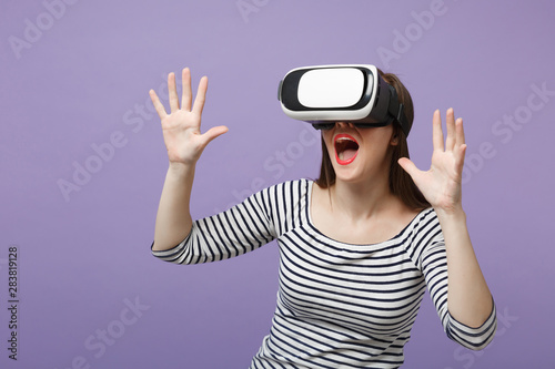 Young brunette woman girl in casual striped clothes posing isolated on violet purple background studio portrait. People sincere emotions lifestyle concept. Mock up copy space. Gesturing in vr headset.