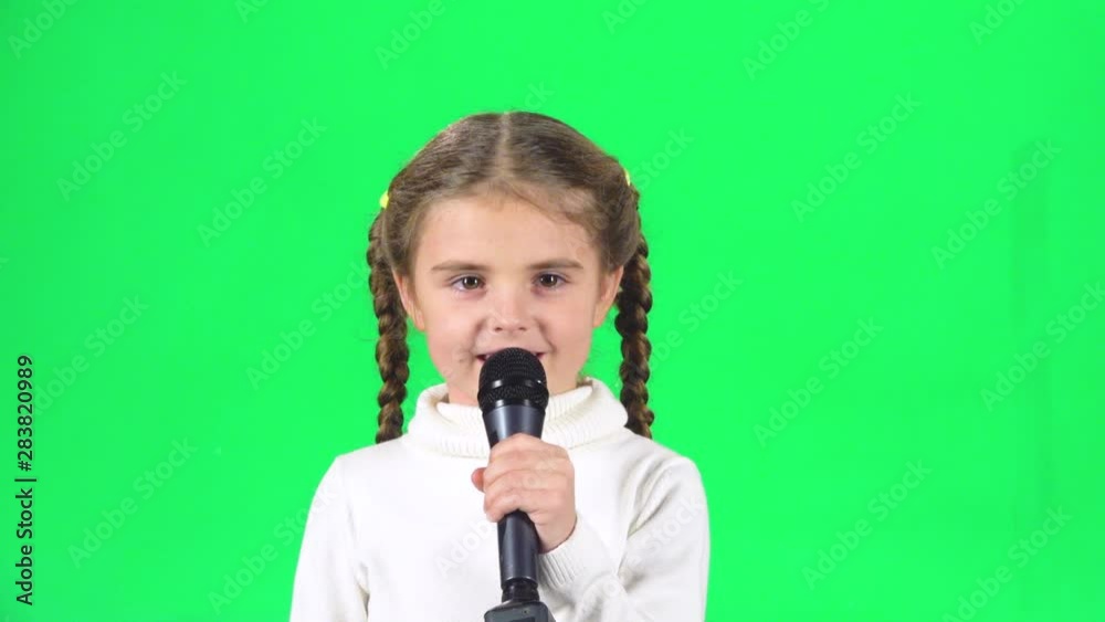 Little girl singing into microphone on green screen at studio. Slow motion Little girl singing into microphone on green screen at studio. Slow motion
