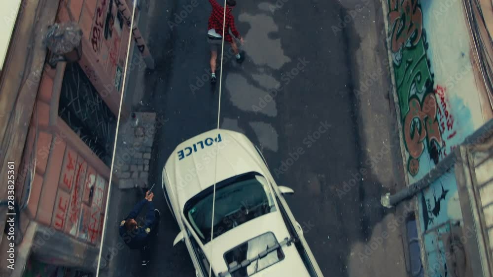 Drone footage impressive scene of young man drug dealer running away from the police in old street. Top down view policemen pursuing dangerous male thief.