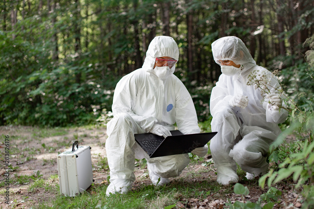 Ecological problem. Pollution. Examine soil. Scientist working in forest in protective mask and suit taking water and soil samples. Chemist makes an analysis of the environment for radiation. Ecological problem. Pollution. Examine soil. Scientist working in forest in protective mask and suit taking water and soil samples. Chemist makes an analysis of the environment for radiation.