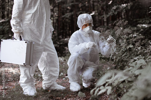 Ecological problem. Pollution. Examine soil. Scientist working in forest in protective mask and suit taking water and soil samples. Chemist makes an analysis of the environment for radiation. 
