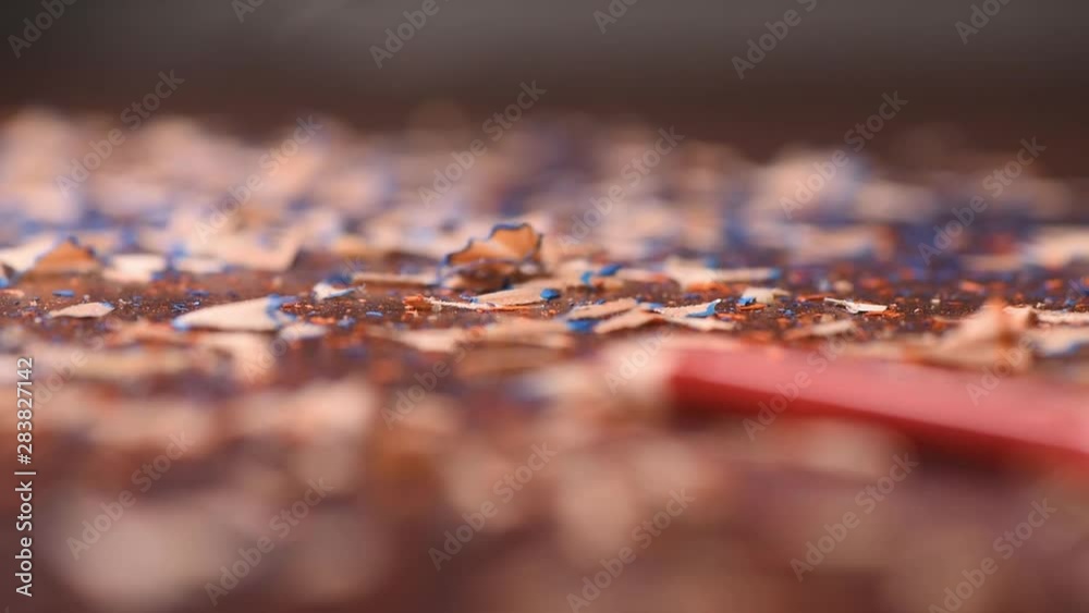 Close-up focus from the fareground with a red pencil to background with a lot of shavings on the table Close-up focus from the fareground with a red pencil to background with a lot of shavings on the table
