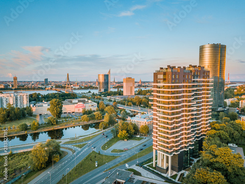 Panoramic, aerial view over Riga city. Modern buildings, roads, and other infrastructure. Cable bridge leading to iconic old town panorama in vivid sunset colors. 
