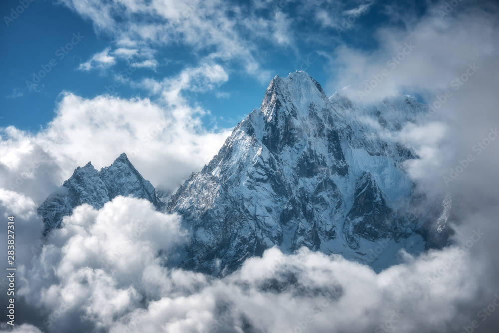 Manaslu mountain with snowy peak in clouds in sunny bright day in Nepal. Landscape with high snow covered rocks and blue cloudy sky. Beautiful nature. Fairy scenery. Aerial view of Himalayan mountains - obrazy, fototapety, plakaty 