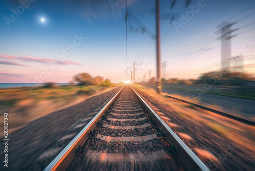 Railroad and beautiful blue sky with full moon at sunset with motion blur effect in summer. Industrial landscape with railway station and blurred background.  Railway platform in speed motion. Concept © den-belitsky