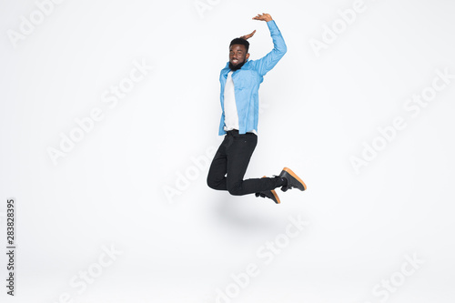 Full length portrait of cheerful handsome joyful afro man wearing casual denim jeans clothing jumping up, isolated on gray background