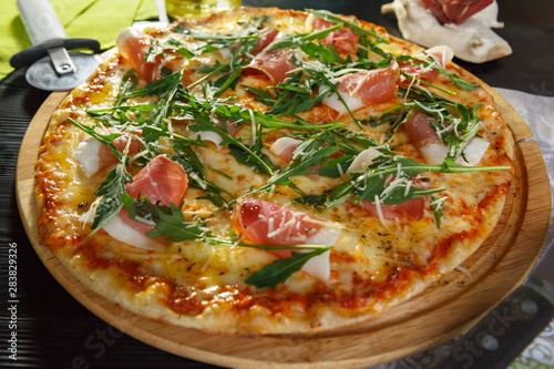 Pizza with bacon, cheese and herbs on a black wooden background