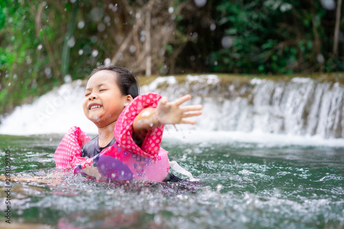 little asian girl wearing inflatable sleeves swimming in nature water on holiday