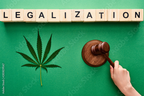 cropped view of woman holding wooden gavel near cannabis leaf and legalization lettering on wooden blocks photo
