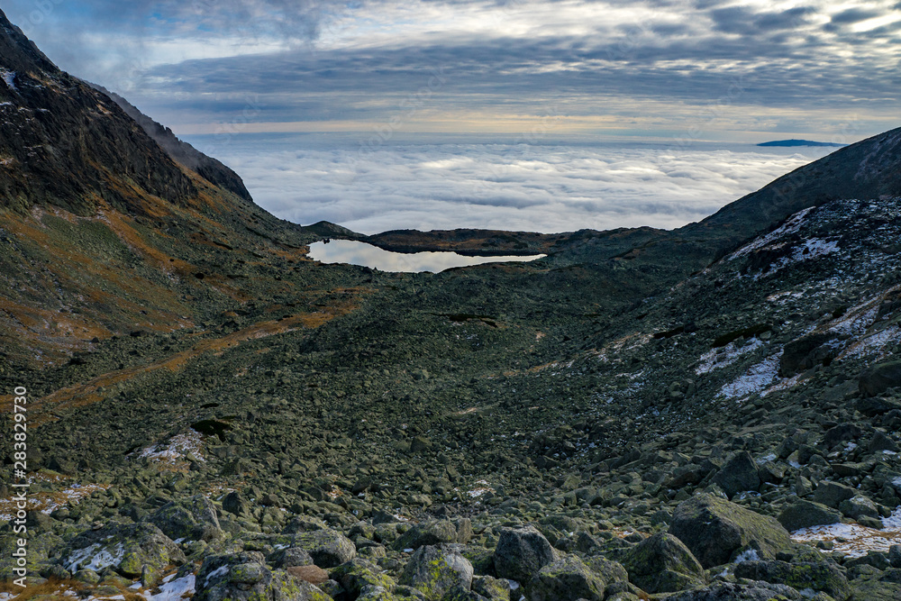 Fototapeta premium High mountains. View of the valley with the lake, many beautiful clouds below and above.