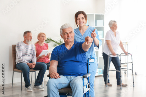 Young caregiver looking after disabled mature man in nursing home