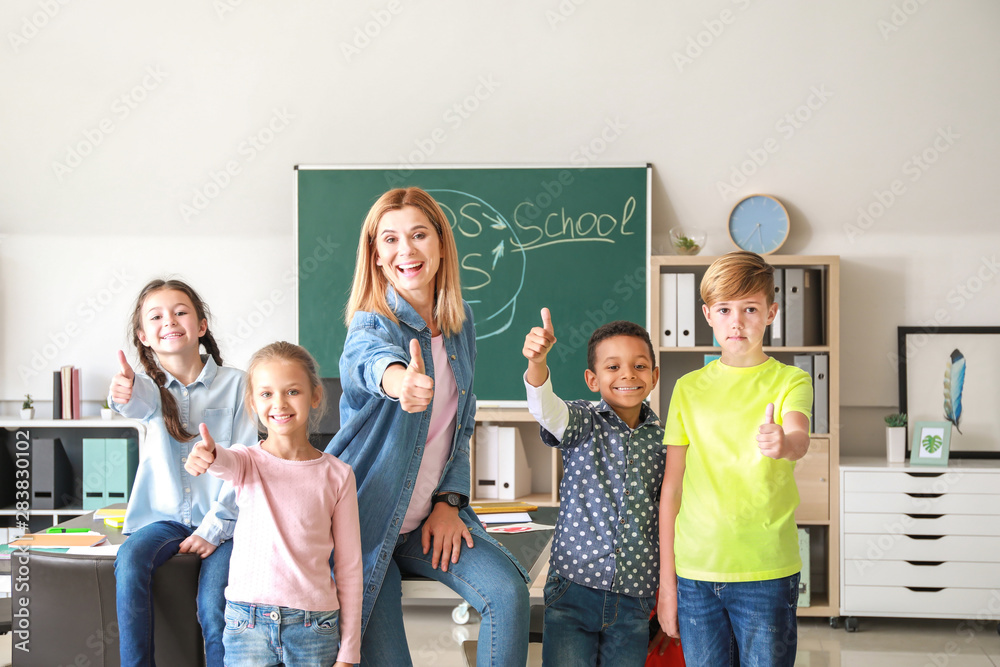 Cute children with teacher showing thumb-up gesture in classroom Cute children with teacher showing thumb-up gesture in classroom