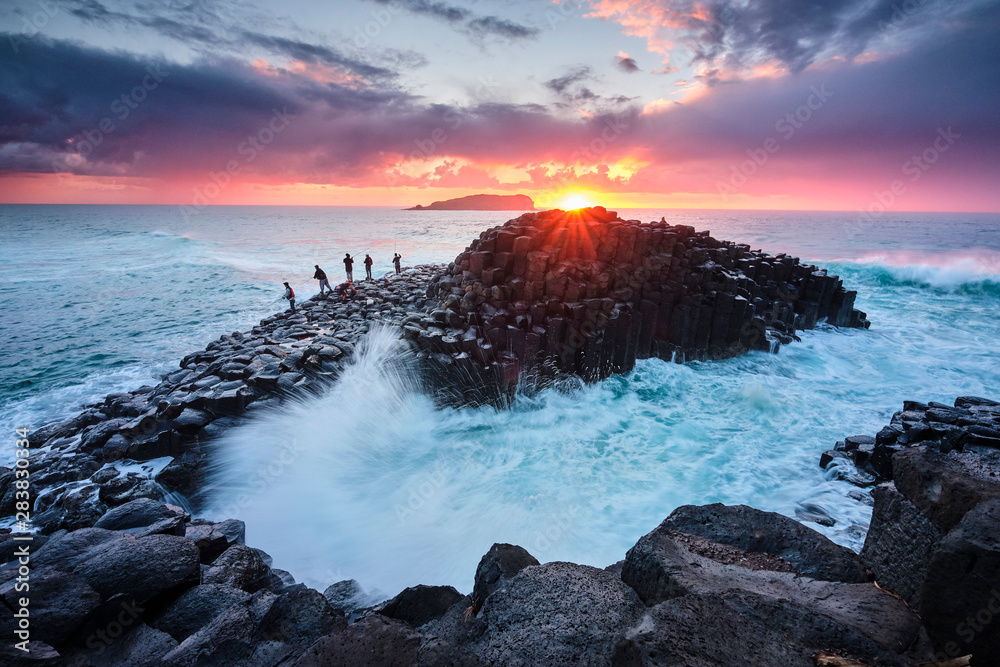 Φωτογραφία Fisherman on Giants Causeway at sunrise with red ball of the sun and nice clouds