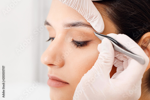 Tableau sur toile Young woman undergoing eyebrow correction procedure in beauty salon, closeup
