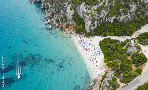 View from above, stunning aerial view of a beautiful beach full of beach umbrellas and people sunbathing and swimming on a turquoise water. Cala Gonone, Sardinia, Italy. photo