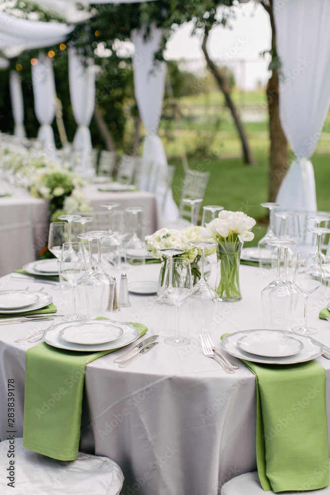 wedding reception table setting, fine china plates, green napkin hanging off table, silverware, wine glasses, and flower arrangments