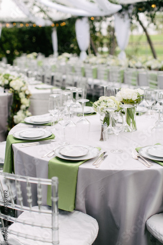 wedding reception table setting  fine china plates  green napkin hanging off table  silverware  wine glasses  and flower arrangments