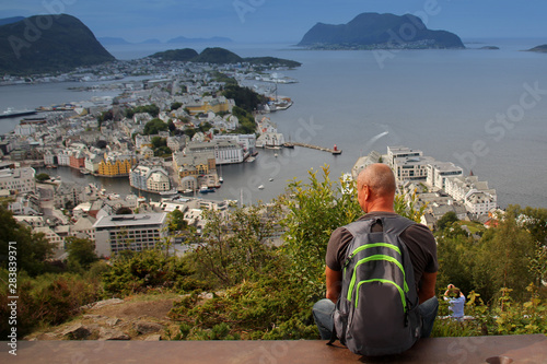 a man is sits on the top of Mount Axla, high above the city of Alesun, Norway photo