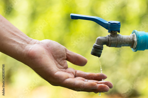 Water from tab pouring in hand on nature background  Concept for save water conservative environment