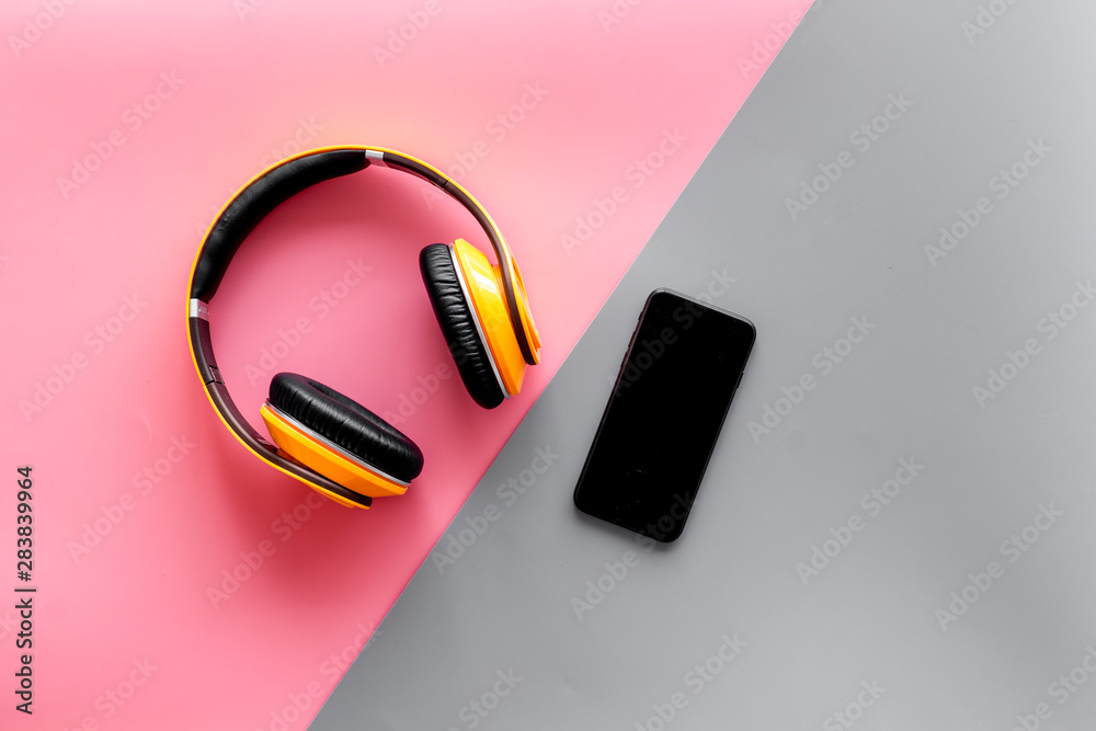 Wireless headphones and mobile phone as music gadgets on pink and gray background top view Wireless headphones and mobile phone as music gadgets on pink and gray background top view